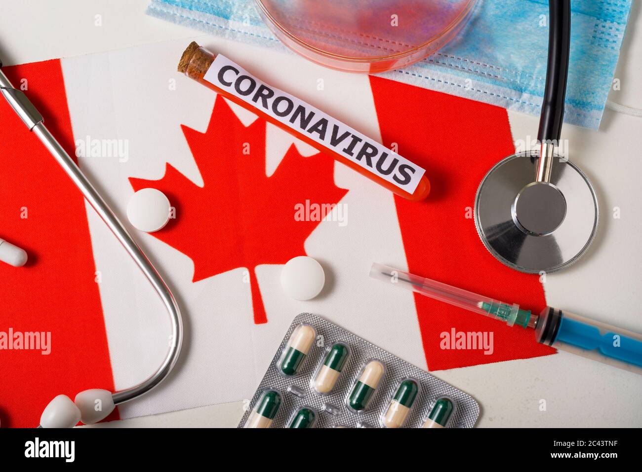 Coronavirus, nCoV concept. Top view protective breathing mask, stethoscope, syringe, pills on the flag of Canada. A new outbreak of the Chinese corona Stock Photo