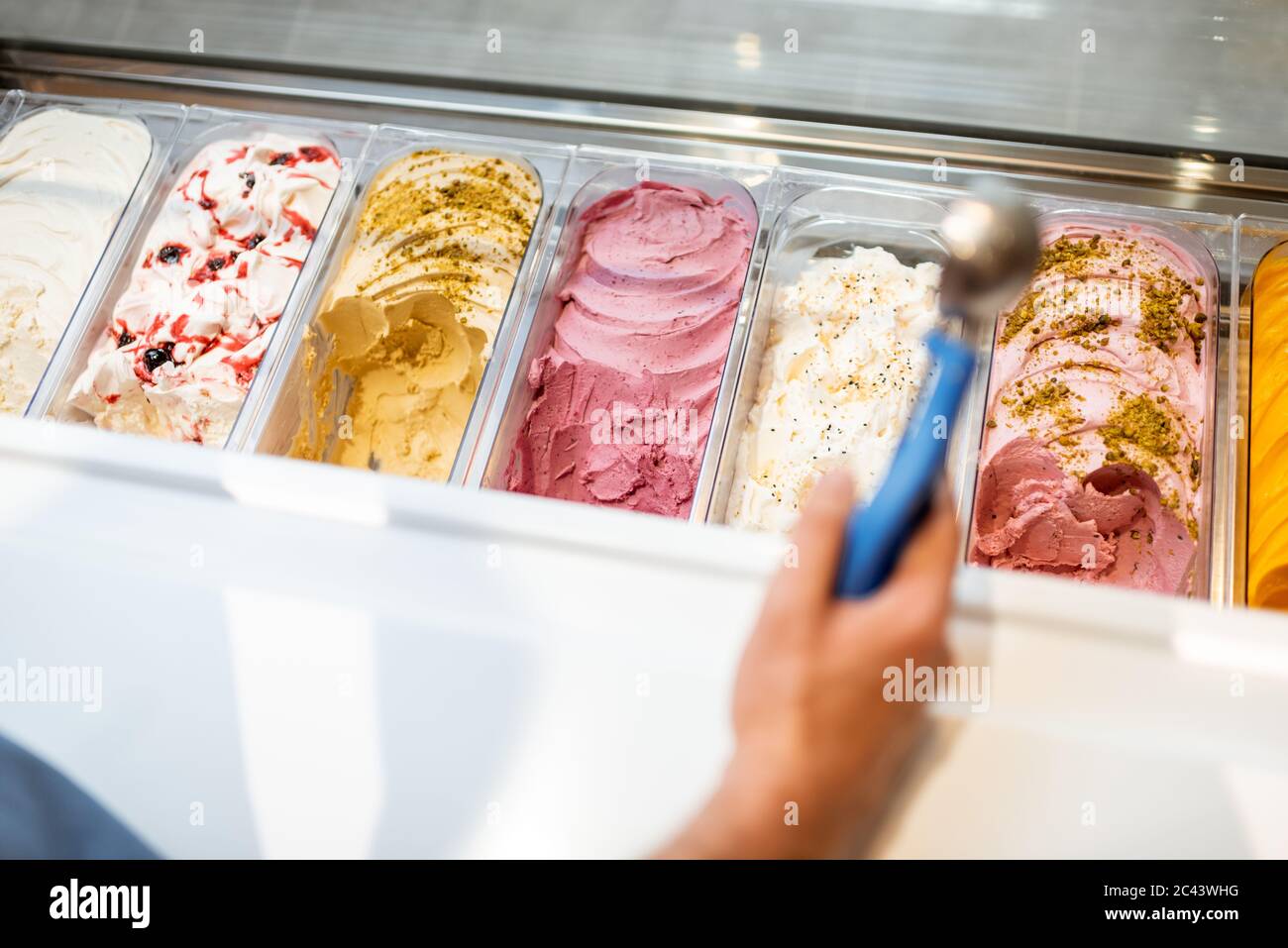 Salesman picking ice cream with a spoon from refrigerator in the store. View from above on a trays full of ice cream with different flavors Stock Photo