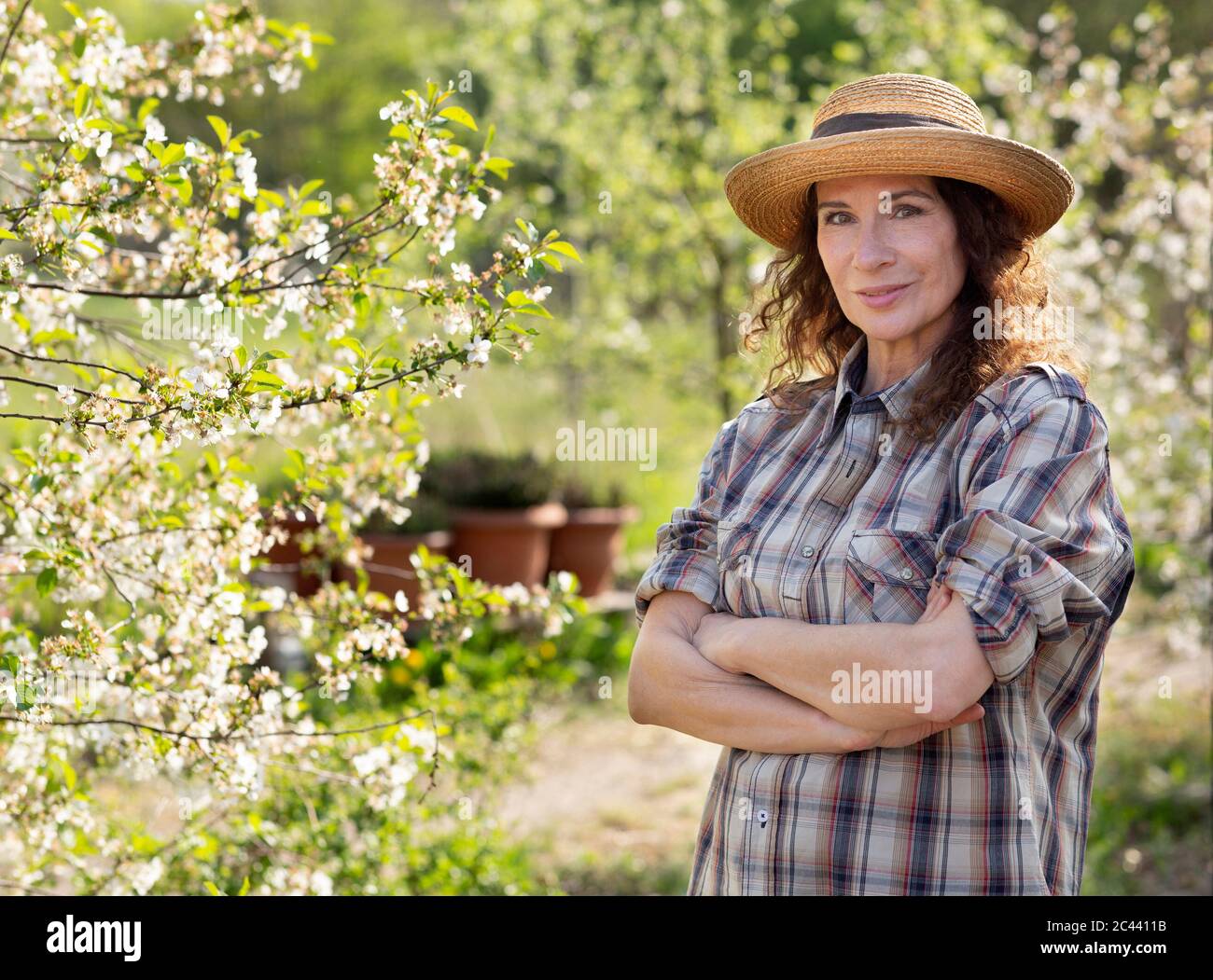 Portrait of smiling mature female farmer standing with arms crossed by ...