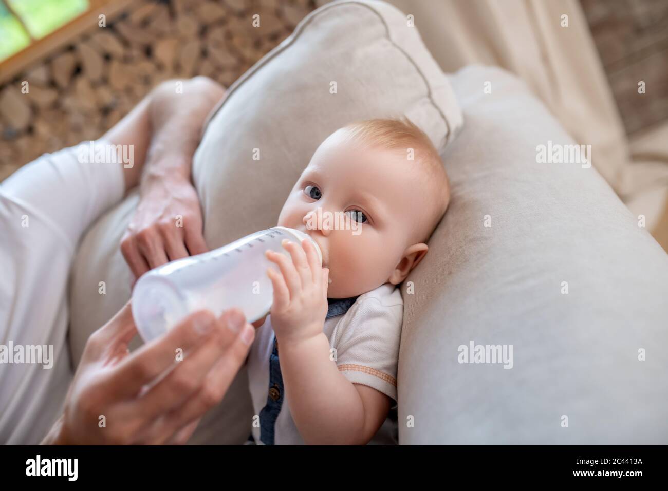 Fathers hands holding the bottle with milk for his little son Stock Photo