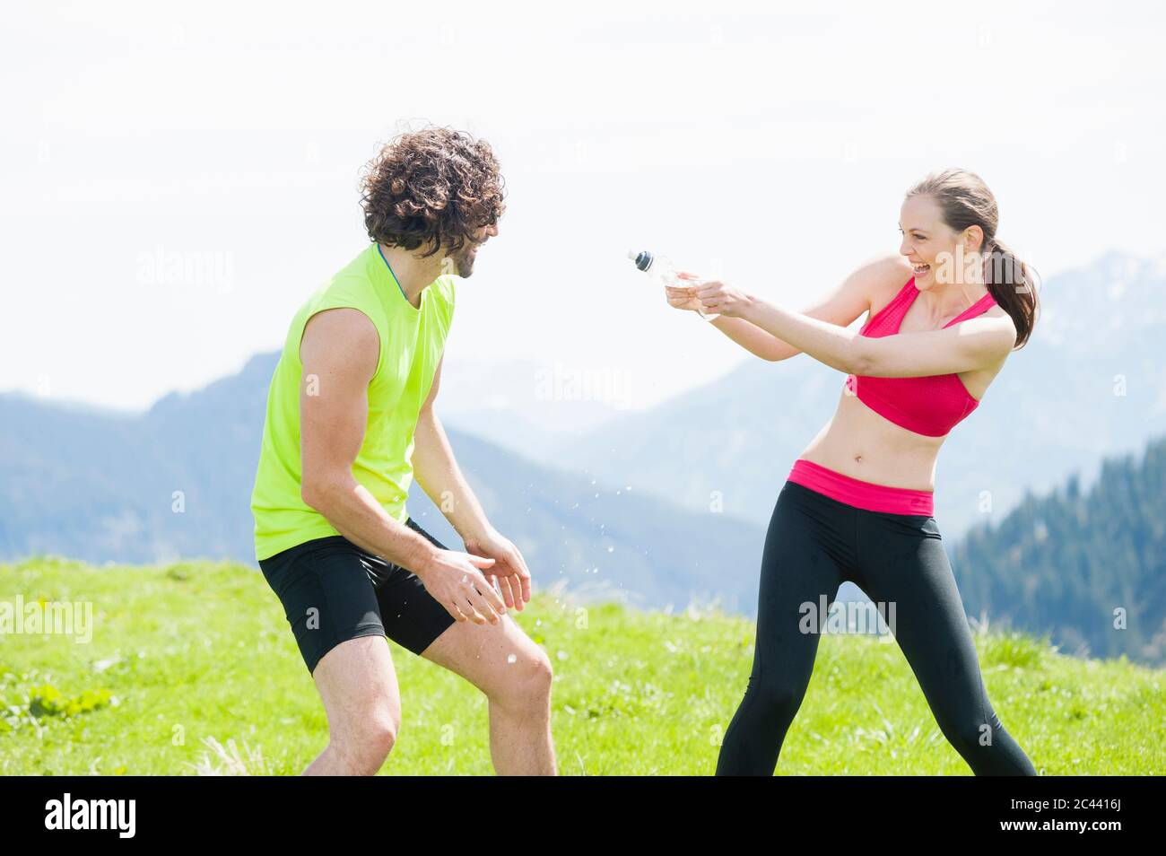 Female jogger squirting water to man, Wallberg, Bavaria, Germany Stock Photo