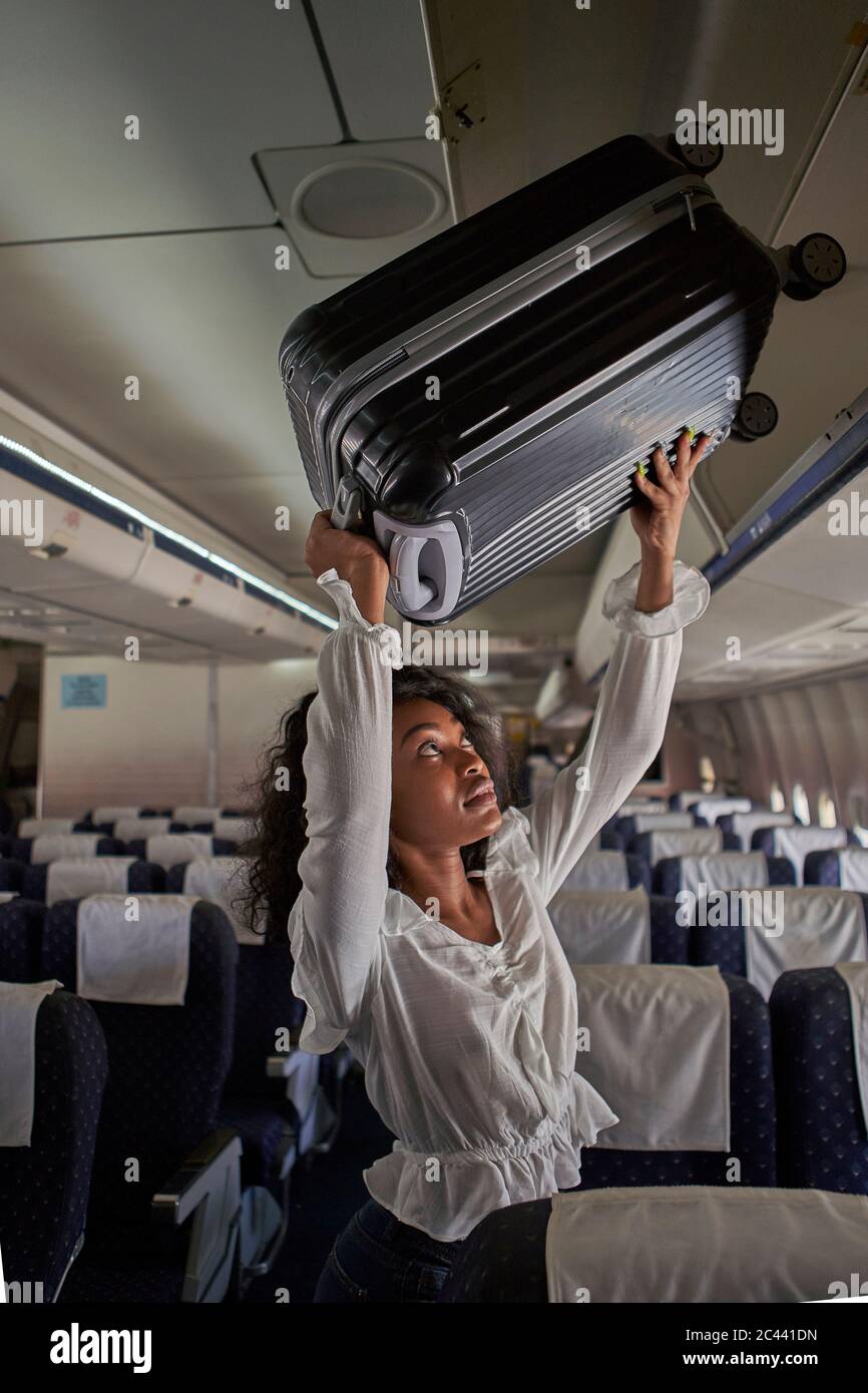 Young woman positioning luggage inside storage compartment in airplane