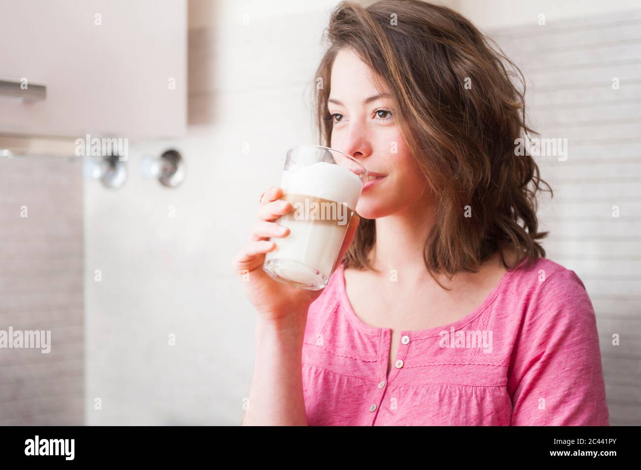 Thoughtful woman drinking Dalgona coffee while standing in kitchen at home Stock Photo