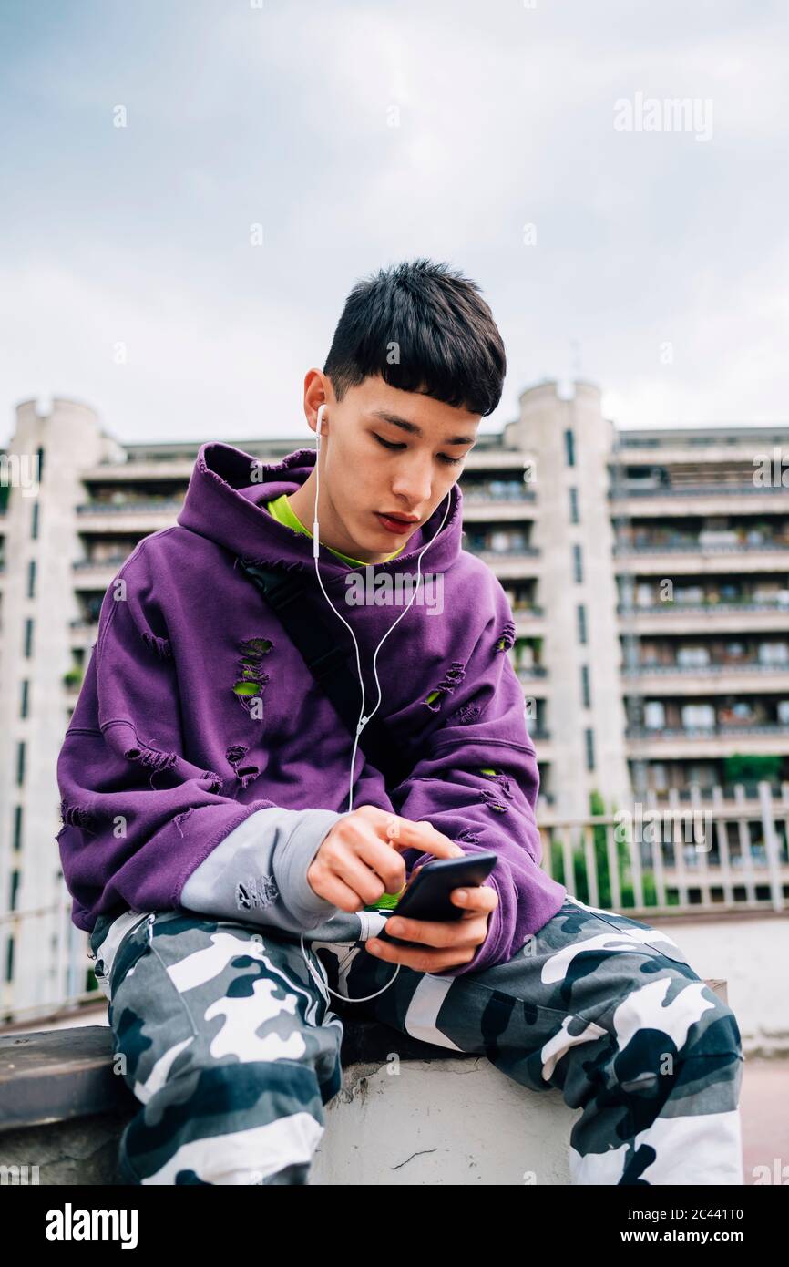 Young man listening music and using smart phone while sitting on seat in city Stock Photo