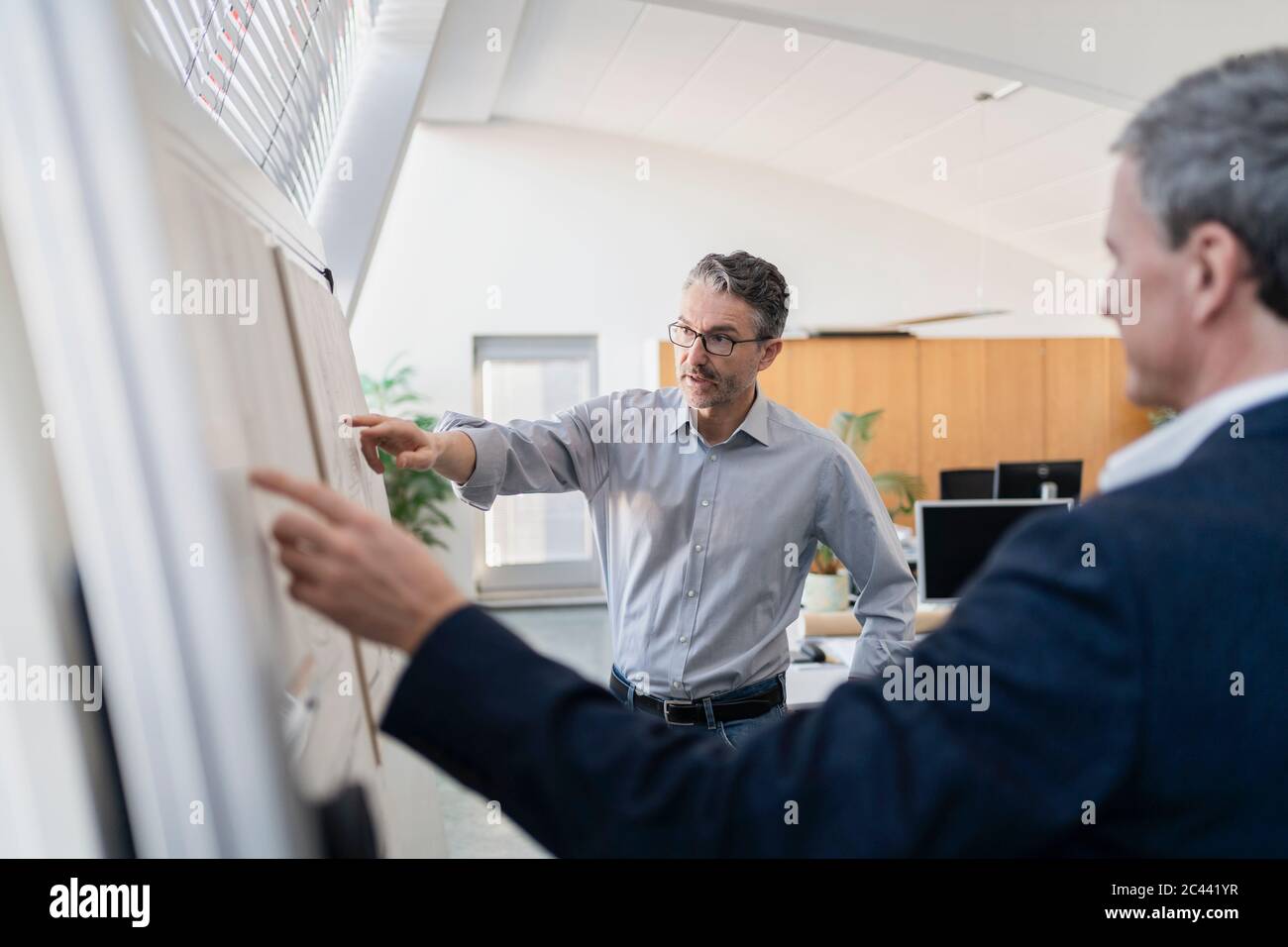 Mature male entrepreneur pointing while explaining strategy to businessman at office during meeting Stock Photo