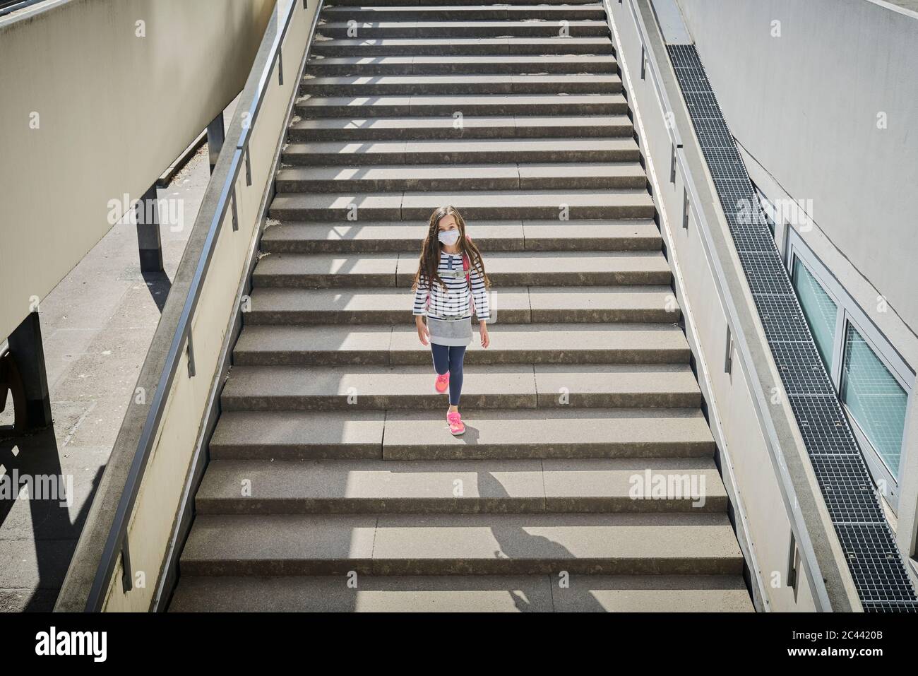 Girl wearing mask and schoolbag walking on stairs Stock Photo