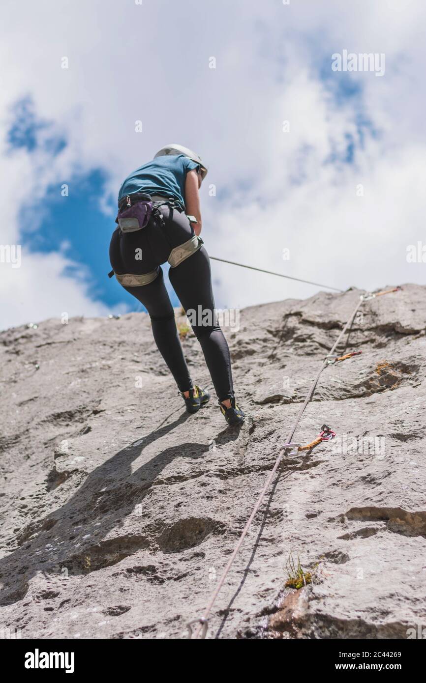 Young woman rappelling down while rock climbing against sky on sunny day Stock Photo