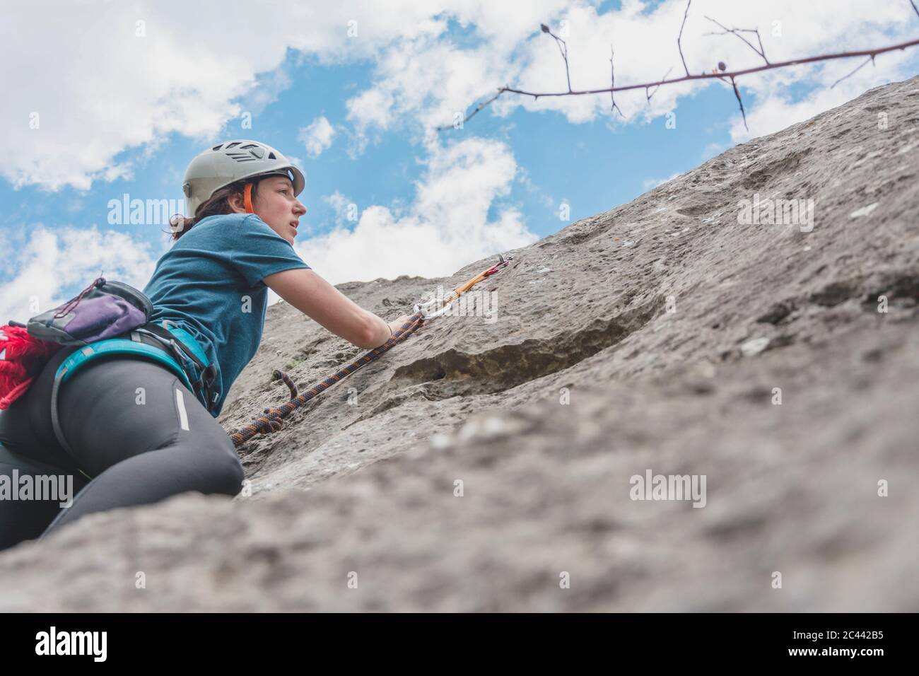 Young woman climbing while looking at rock against sky Stock Photo