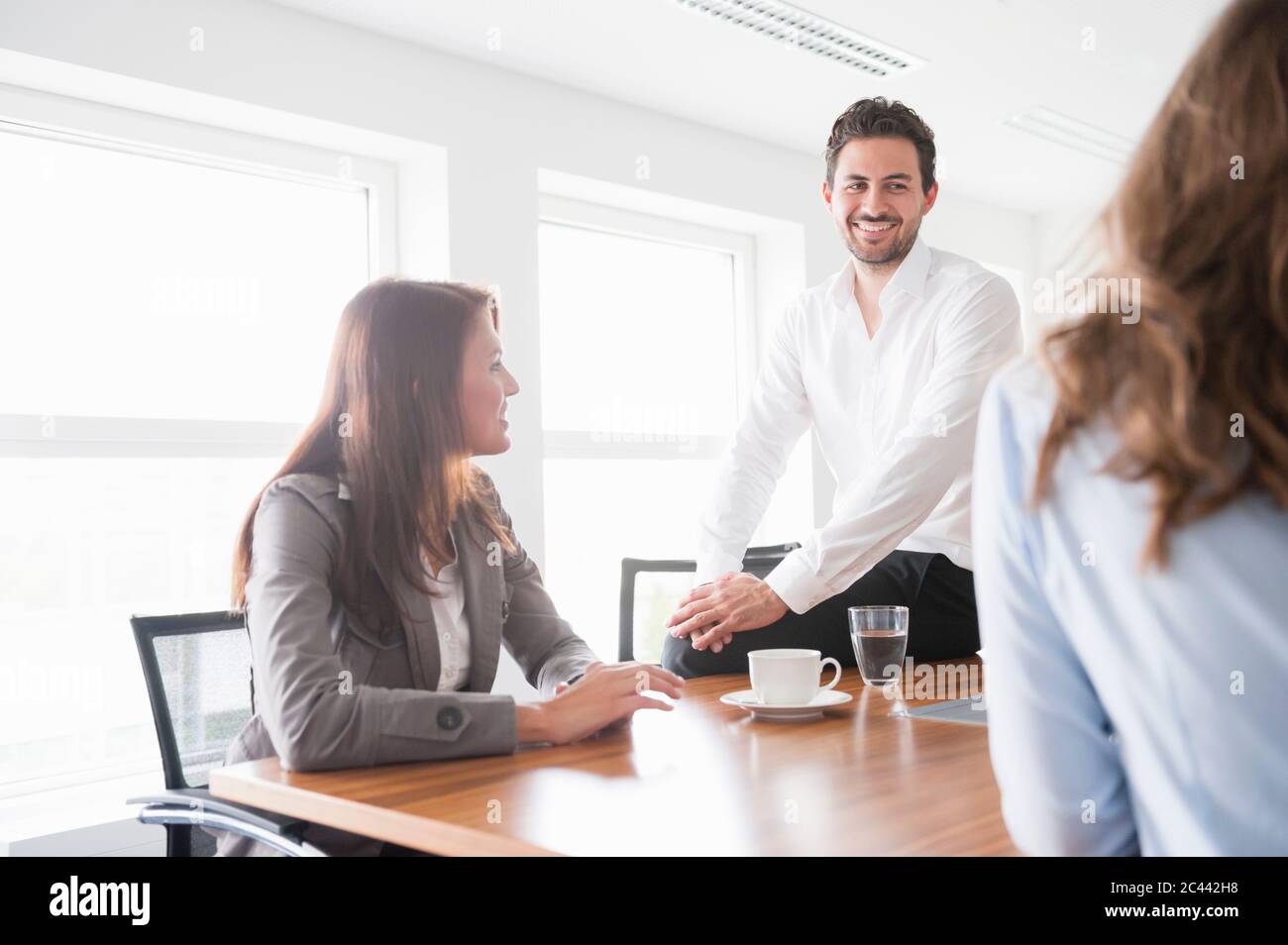 Happy business colleagues discussing in brightly lit board room Stock Photo