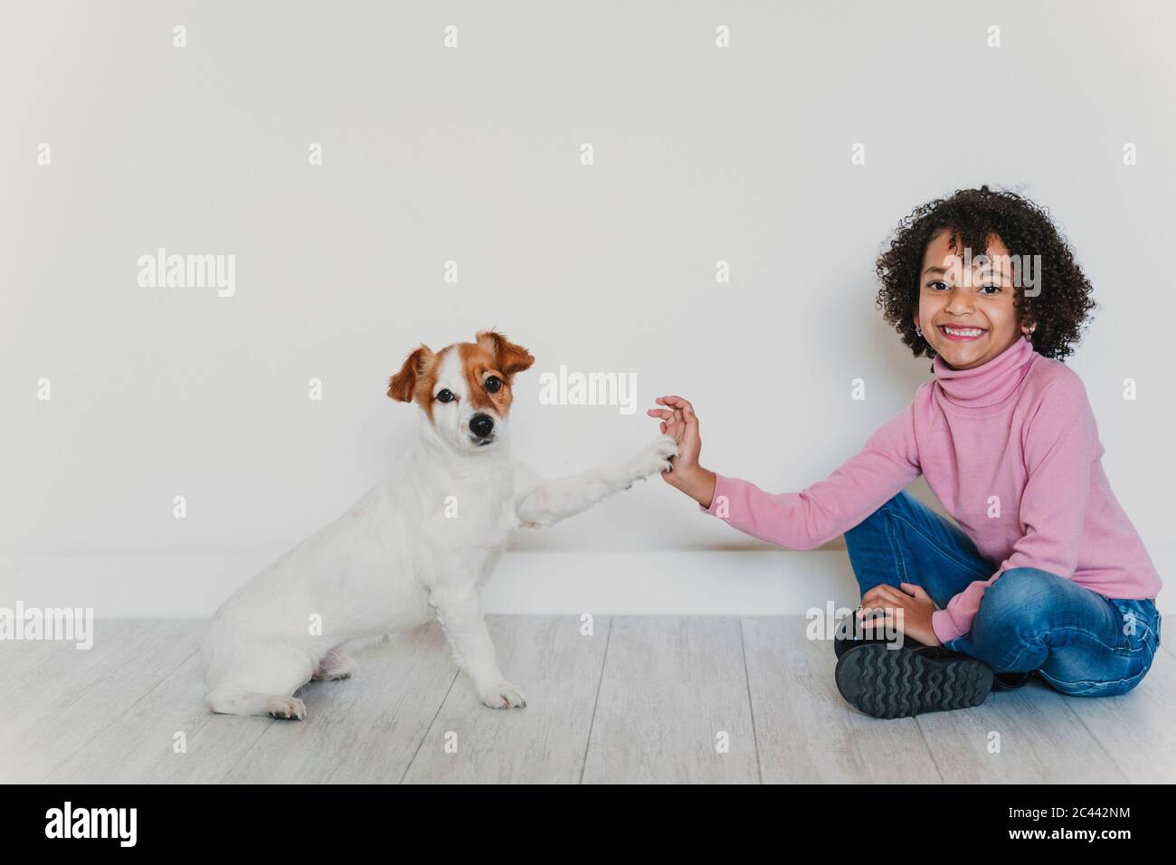 Portrait of smiling little girl sitting on the floor with her dog ...