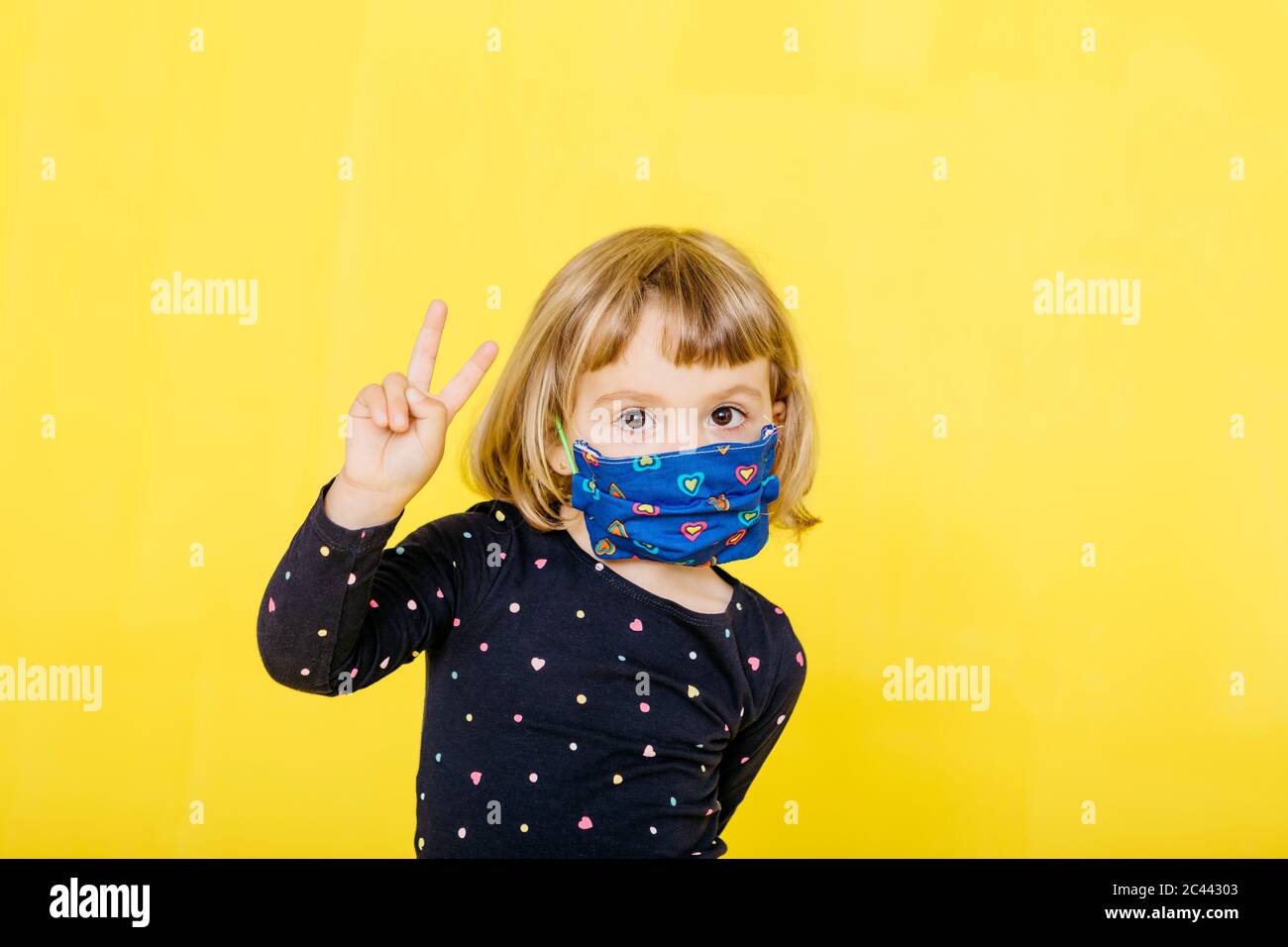 Portrait of cute blond girl wearing face mask and gesturing peace sign