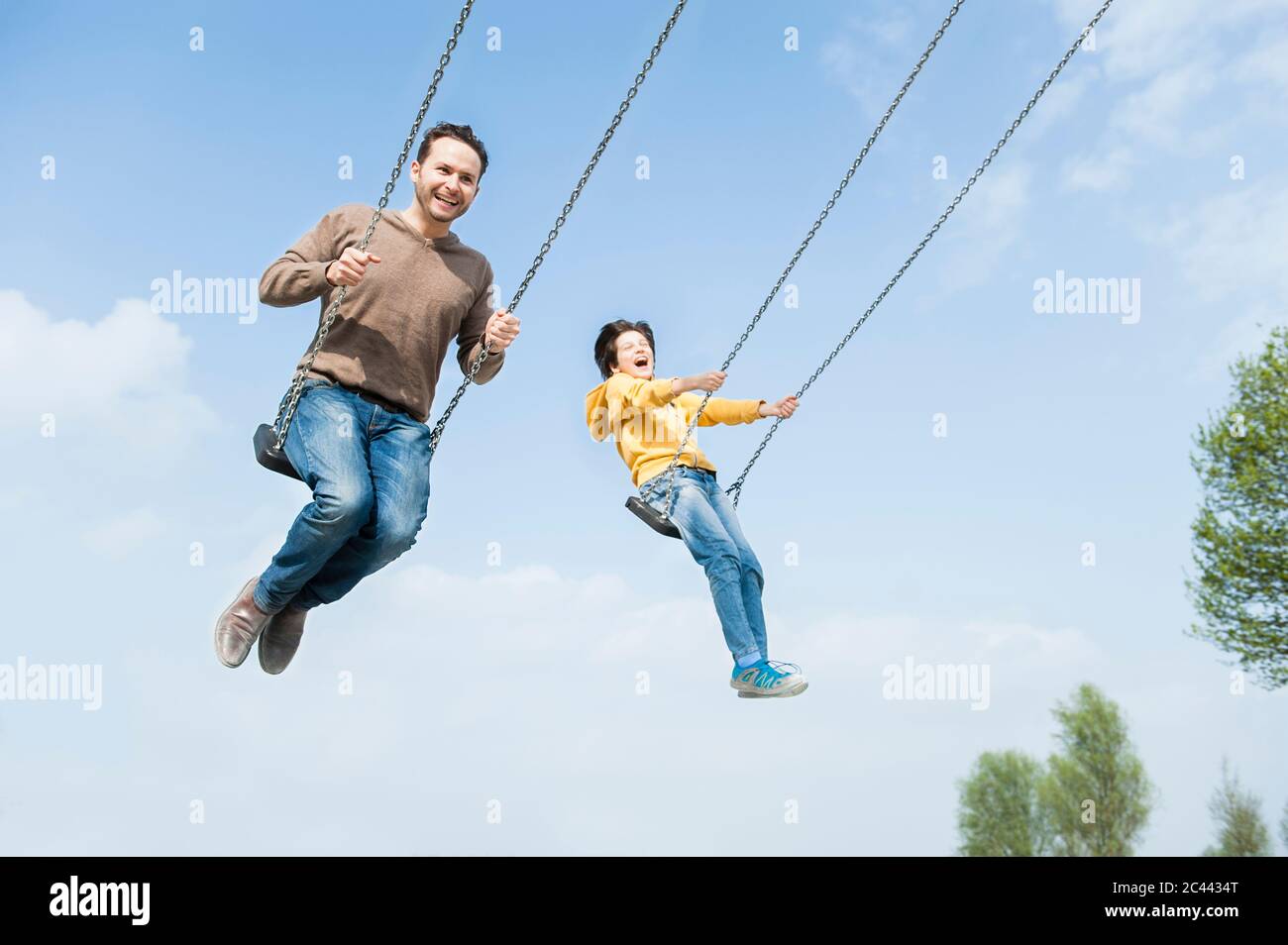 Cheerful father and son swinging against blue sky Stock Photo