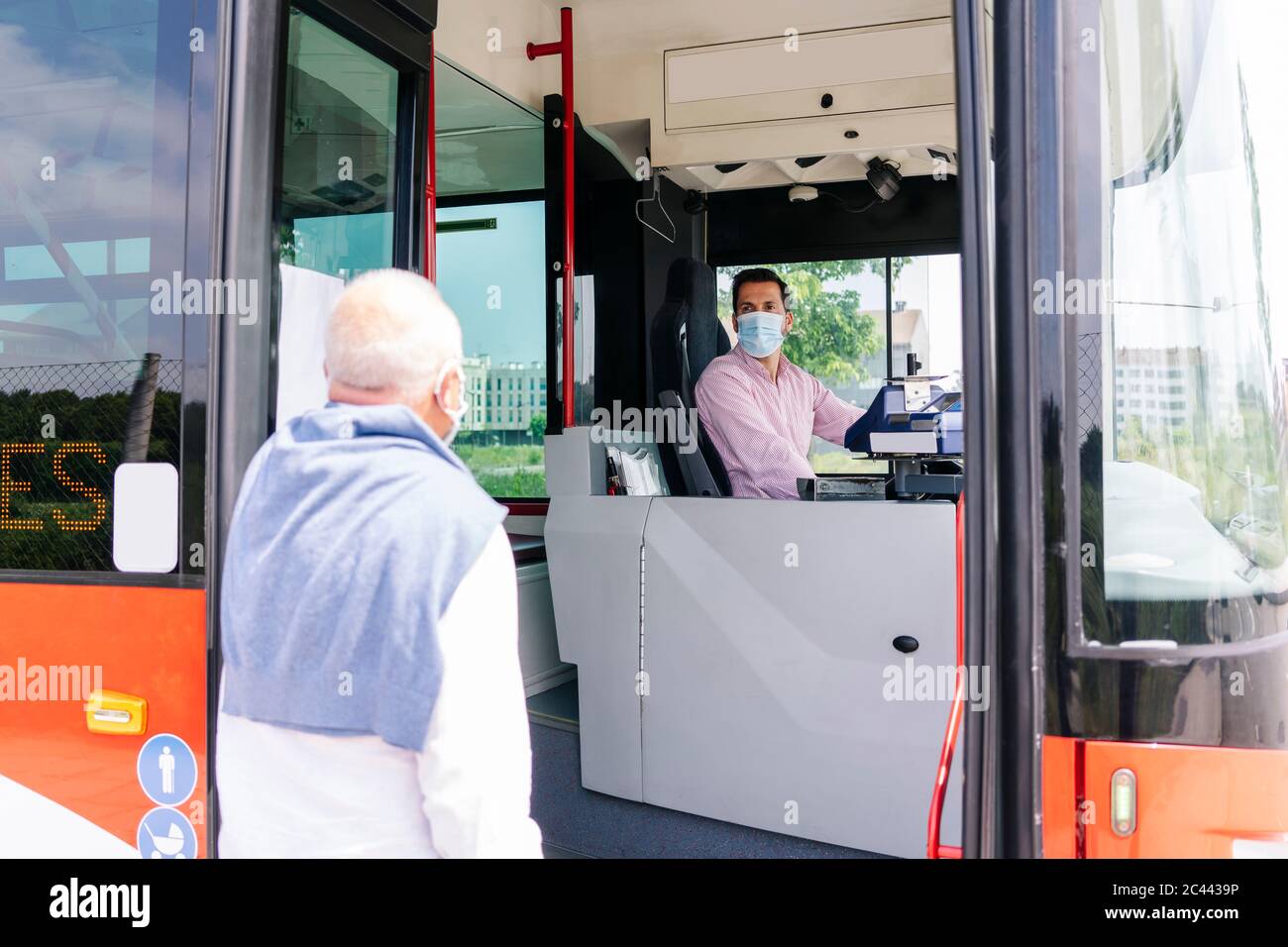 Bus driver wearing protective mask talking to passenger at bus stop, Spain Stock Photo