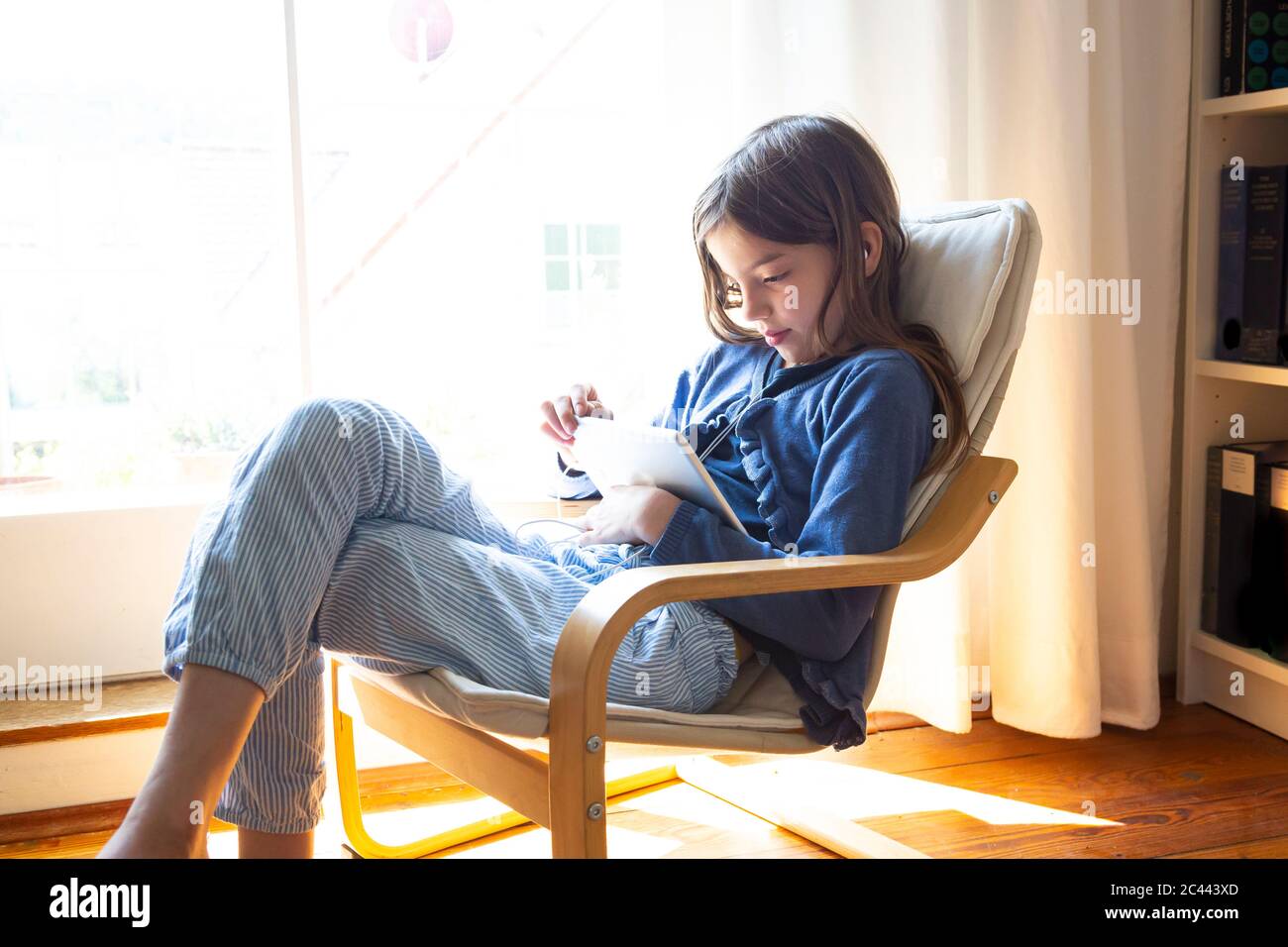 Young girl watching video online on digital tablet while sitting by window at home Stock Photo