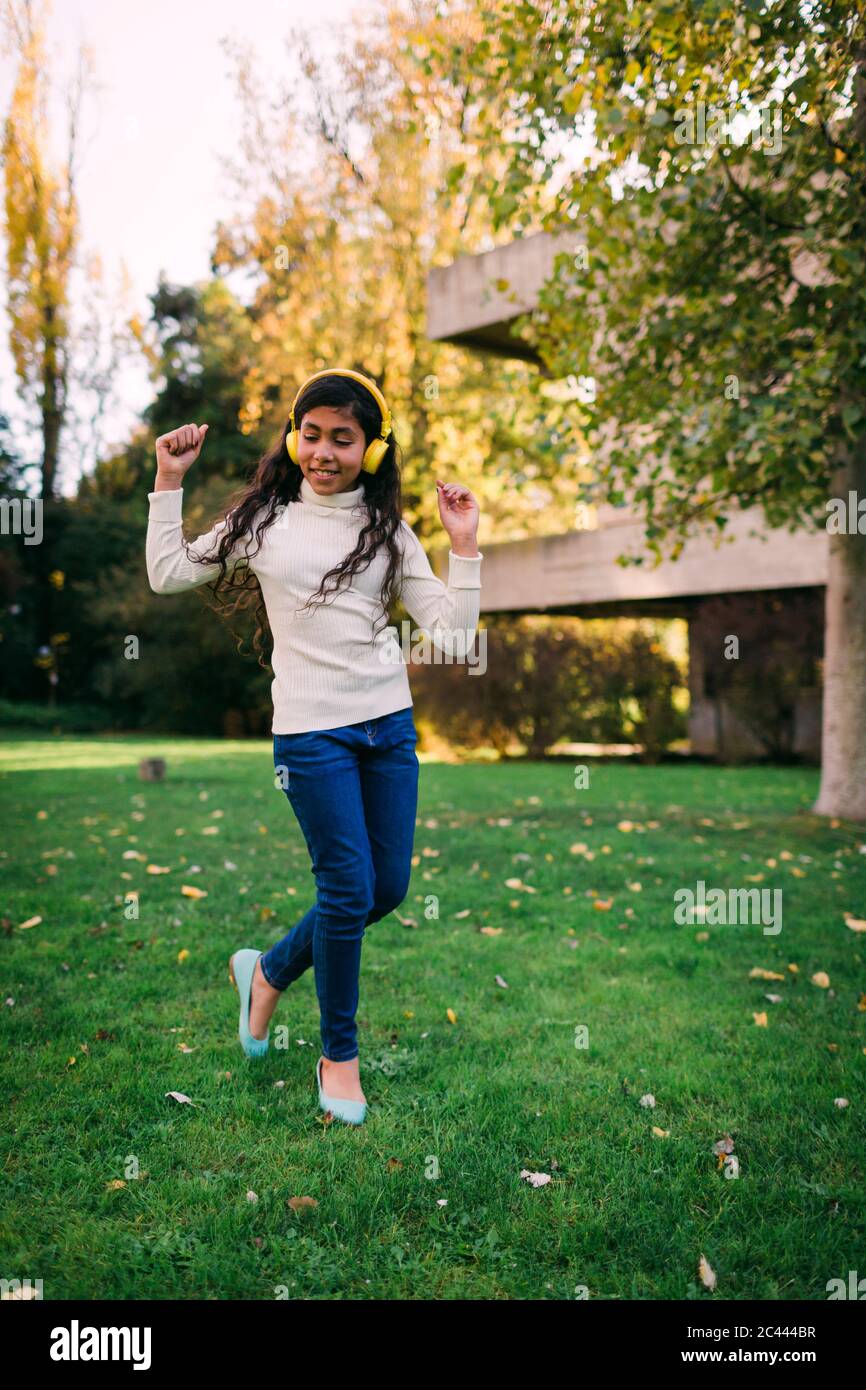 Happy girl listening music and dancing on grassy land in park during autumn Stock Photo