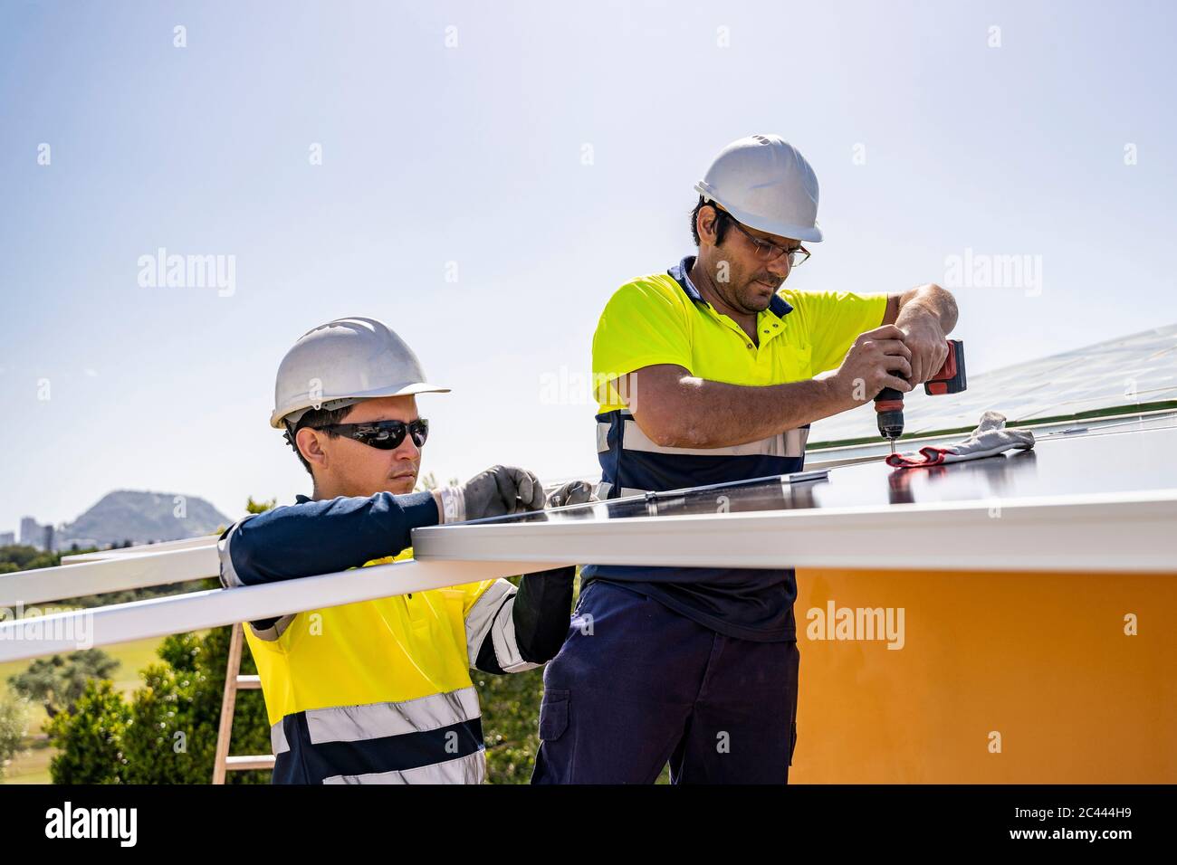 Male technicians installing solar panels on house roof against sky during sunny day Stock Photo