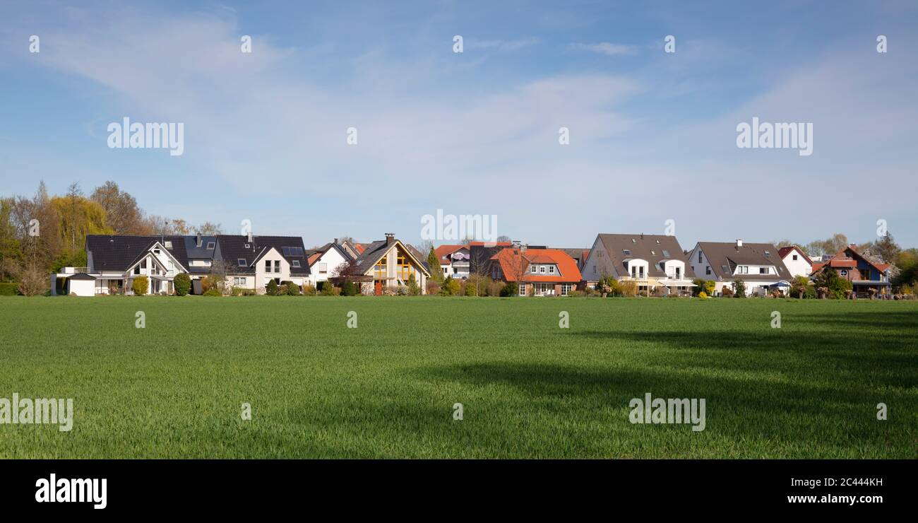 Germany, North Rhine-Westphalia, Kamen, Panorama of green meadow in front of rural houses Stock Photo