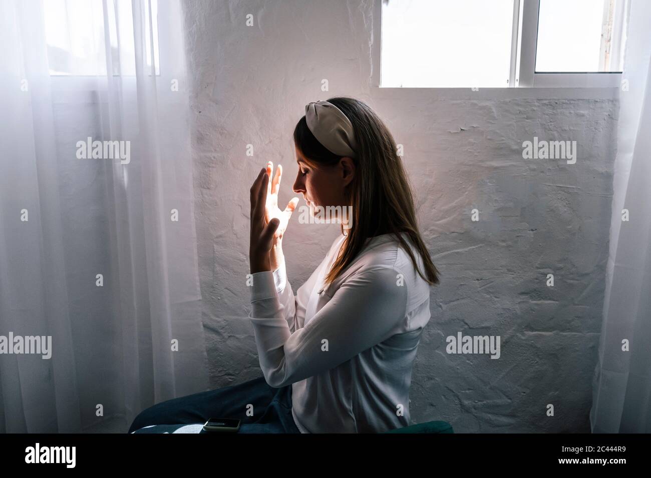 Woman praying by window at home Stock Photo