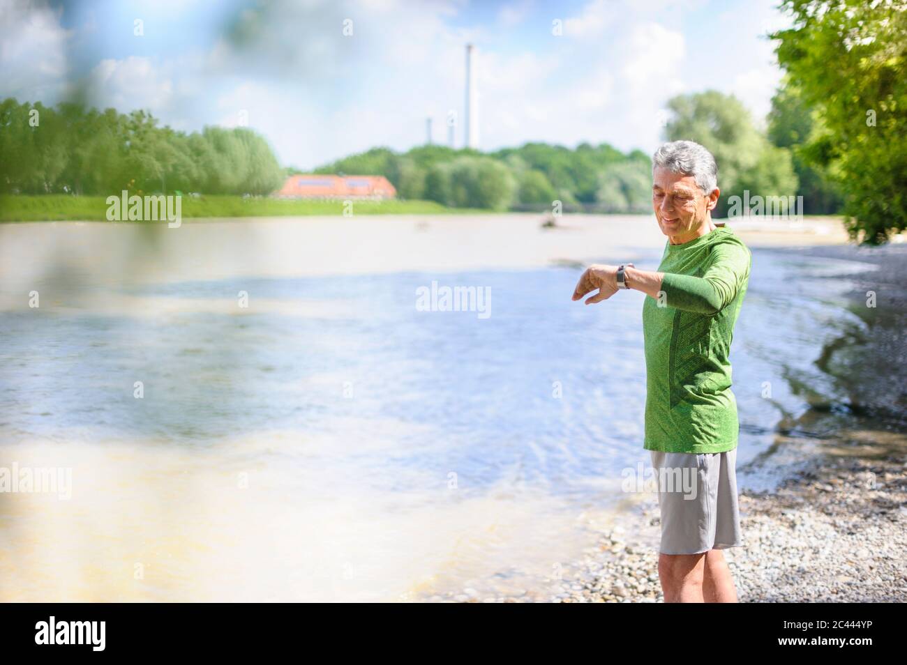 Active elderly man checking time while standing at riverbank on sunny day Stock Photo
