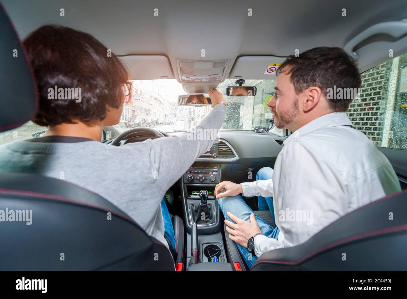 Learner driver with instructor in car, woman adjusting rear view mirror Stock Photo