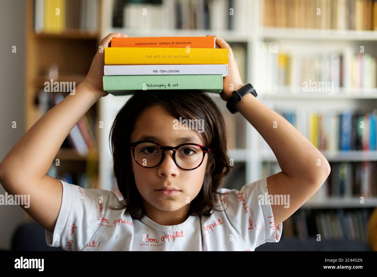 Portrait of serious boy with stack of books on his head Stock Photo