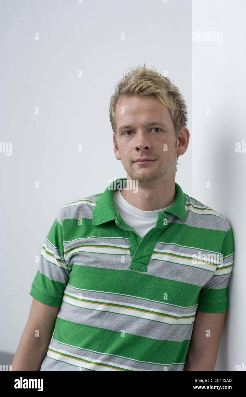 Blond young man leaning against a wall, portrait Stock Photo - Alamy