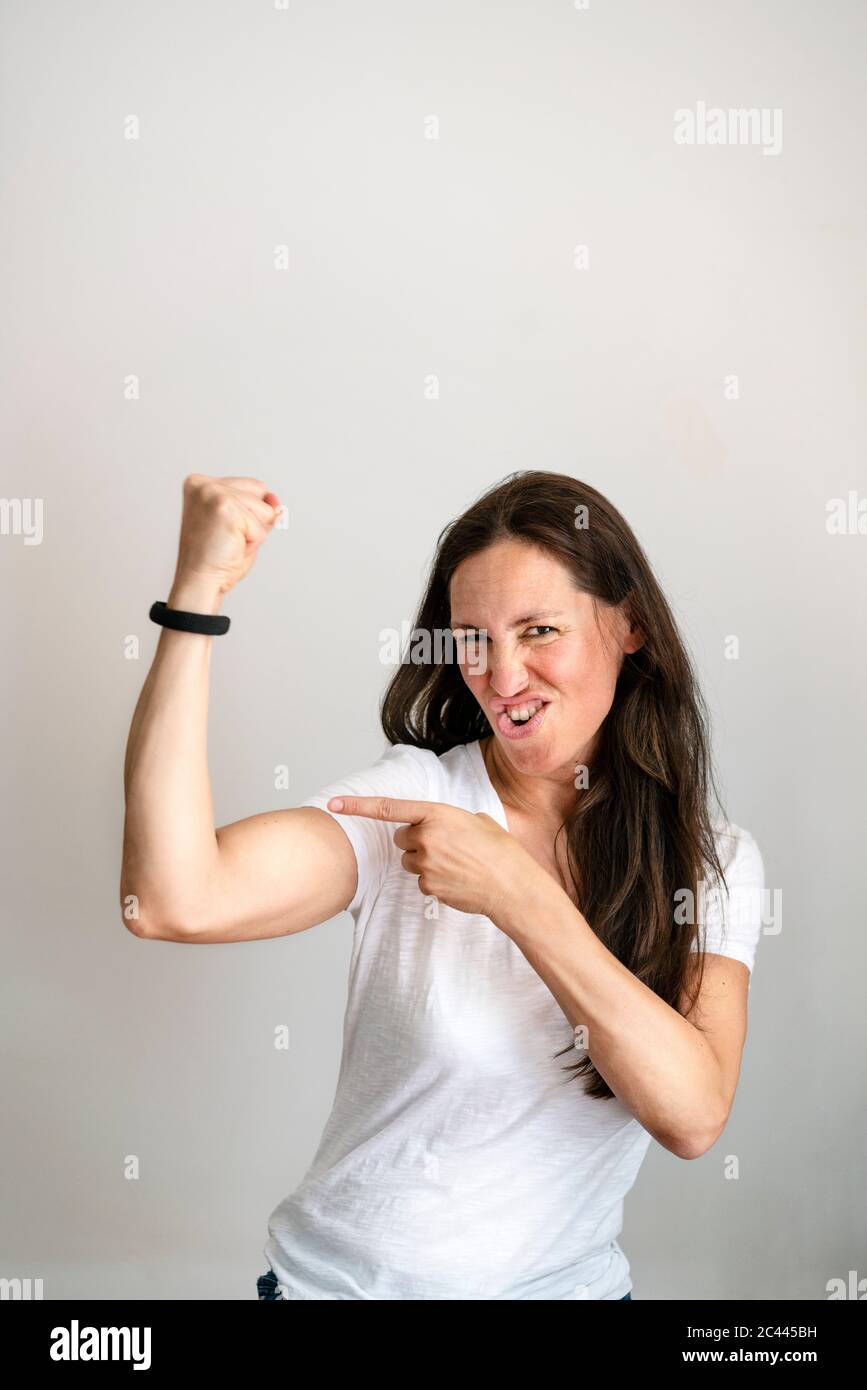 Portrait of cheerful mature woman pointing at bicep against white background Stock Photo