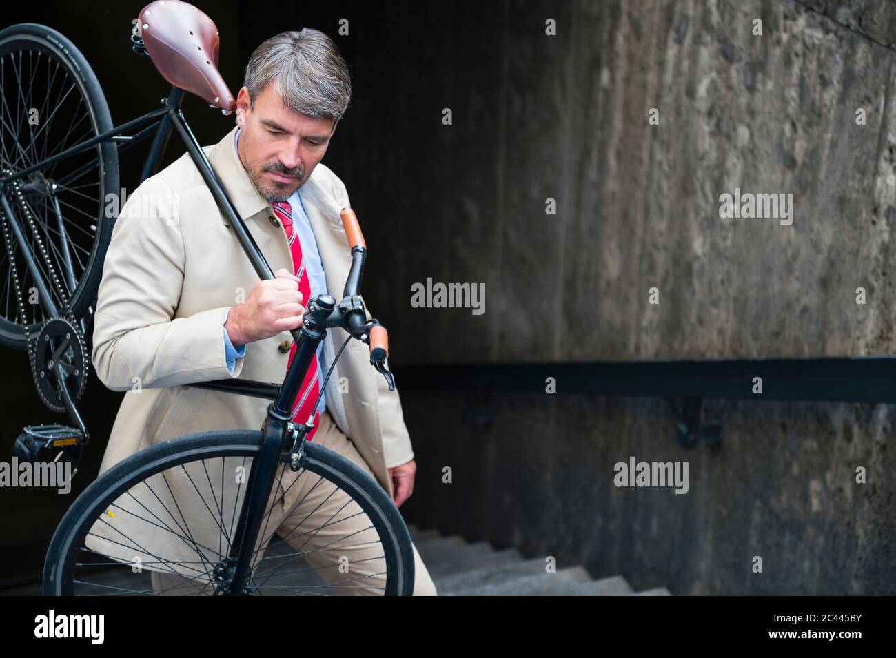 Businessman carrying bicycle while moving up on steps Stock Photo