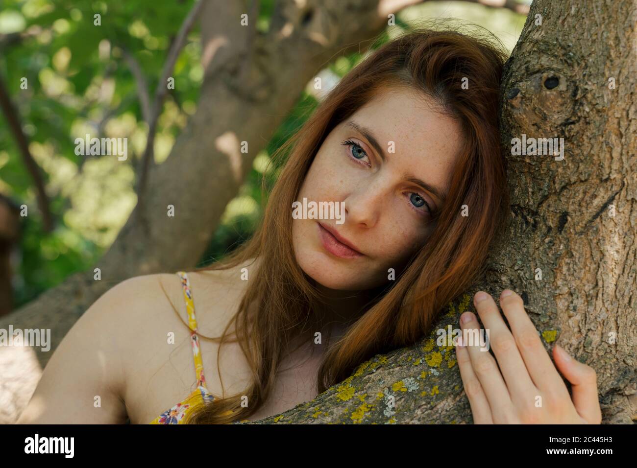 Thoughtful young woman looking away while leaning on tree trunk in garden Stock Photo