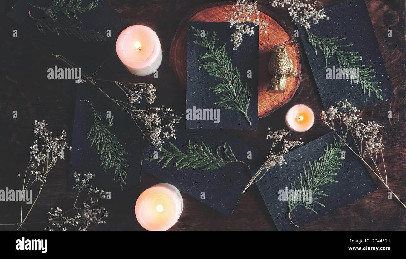 Flat lay of home made diy festive black Yule (Christmas) cards with dried cedar branch glued on it. Natural decoration, burning candles Stock Photo