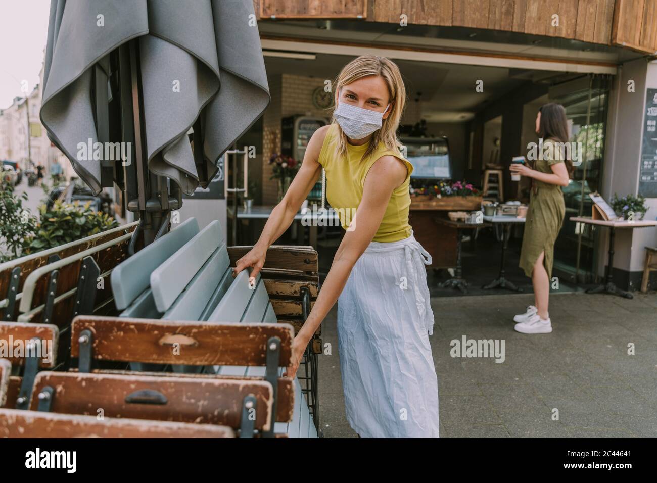 Cafe owner wearing face mask putting up tables and chairs Stock Photo