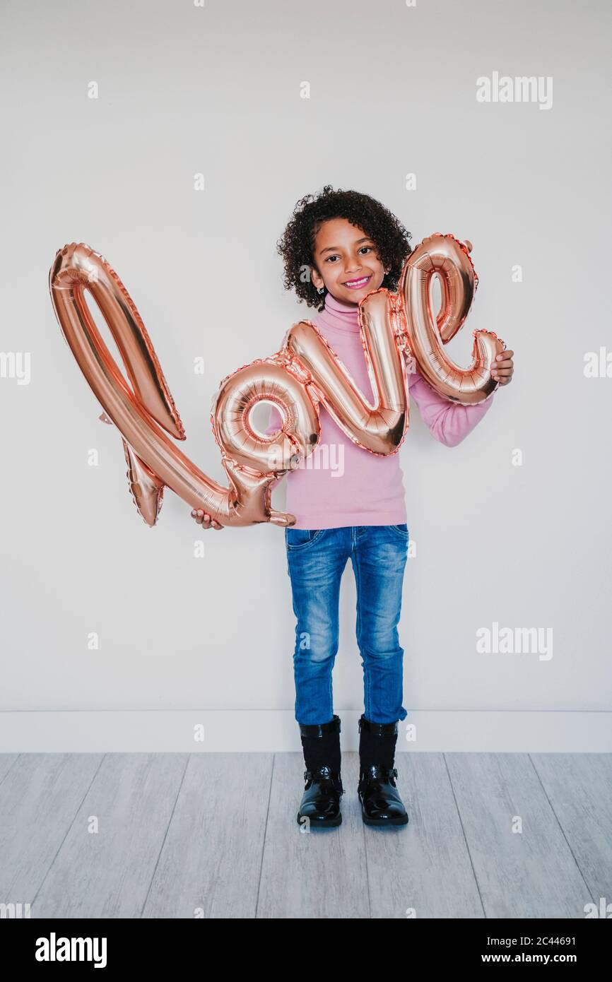 Portrait of smiling girl holding 'love' foil balloon Stock Photo