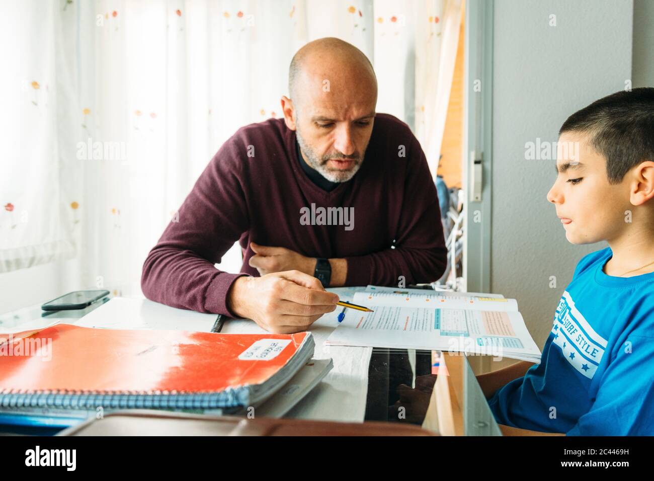 Confident father teaching son while sitting at desk during homeschooling Stock Photo