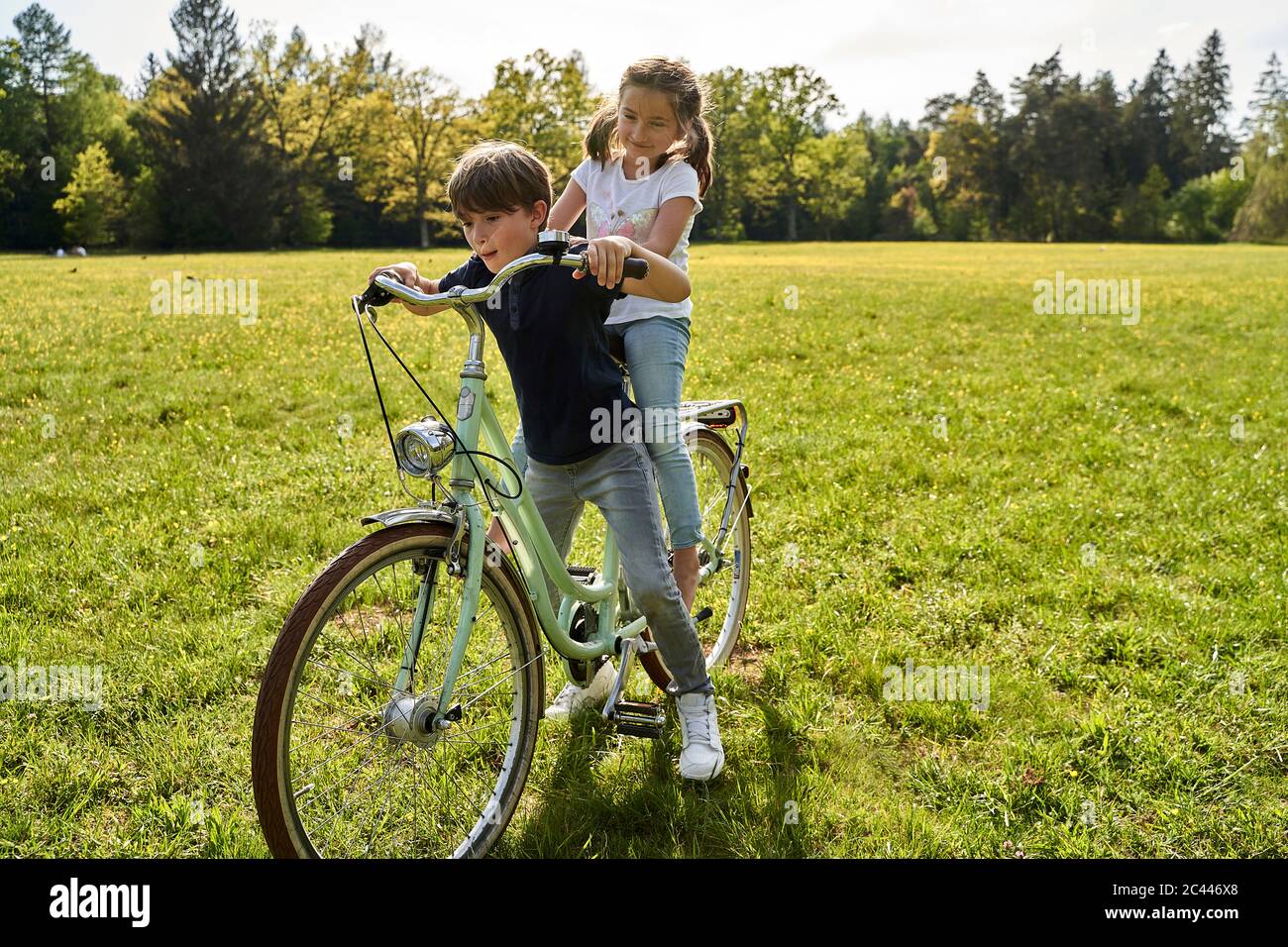 Siblings enjoying bicycle ride on grass during sunny day Stock Photo
