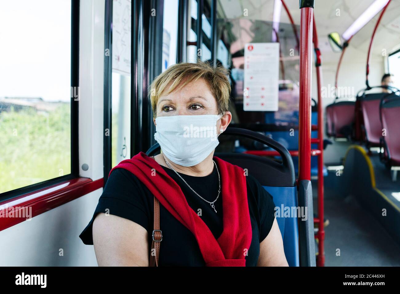 Portrait of mature woman wearing protective mask in public bus looking out of window, Spain Stock Photo