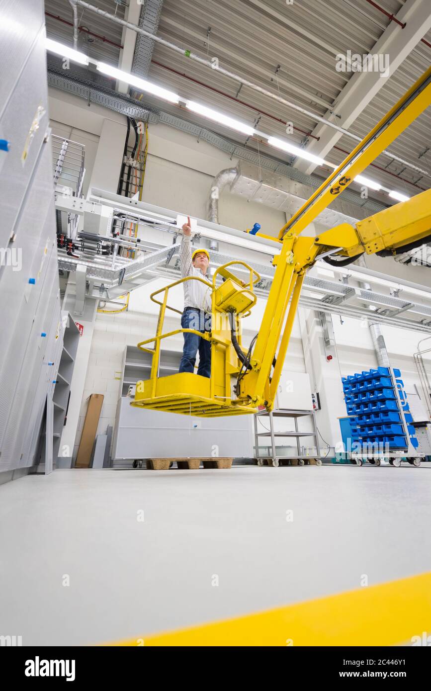 Man wearing hard hat standing on hoist in a factory Stock Photo