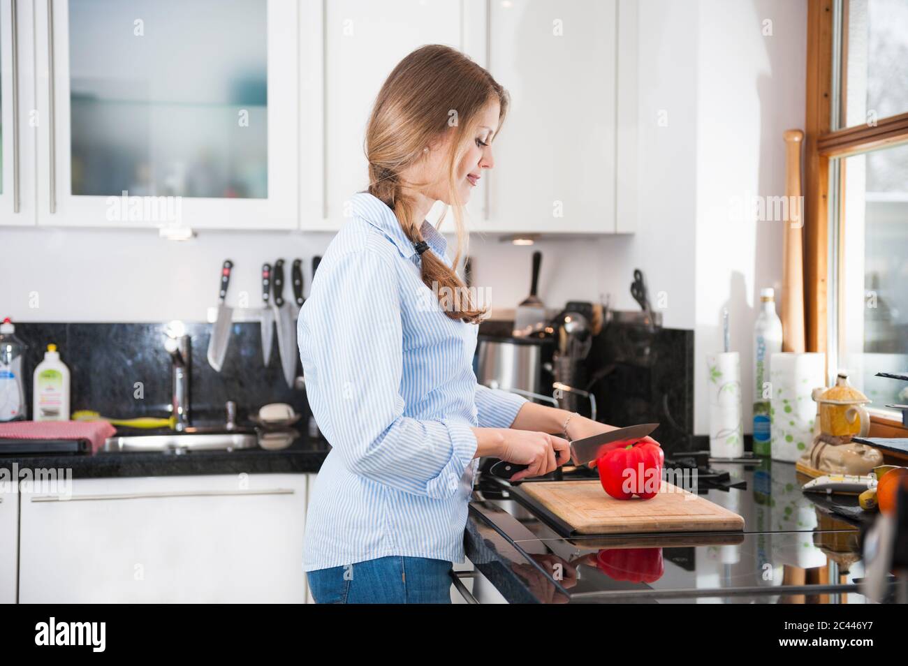 Young woman cutting red bell pepper at kitchen counter Stock Photo