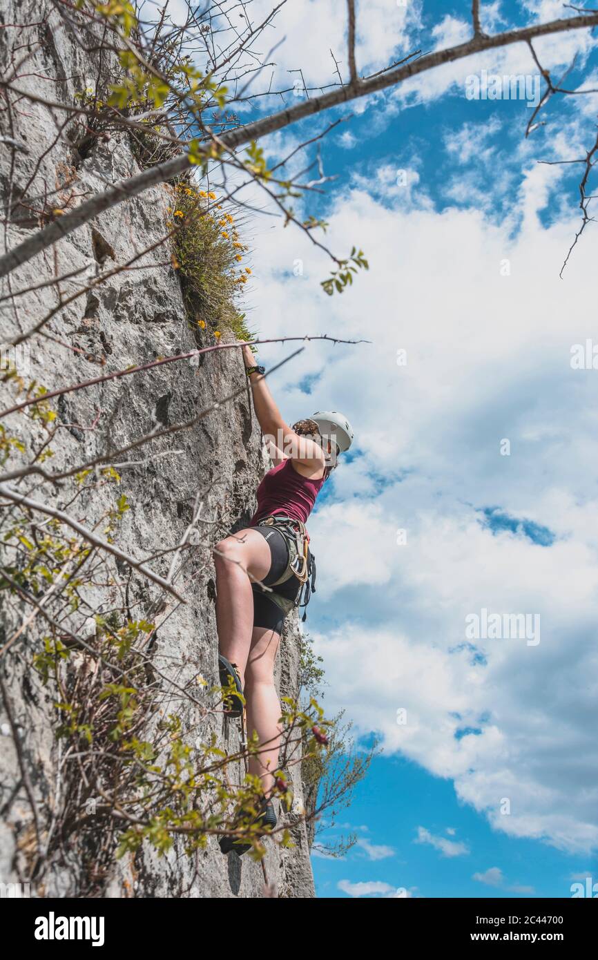 Determined young woman moving up while rock climbing against sky Stock Photo