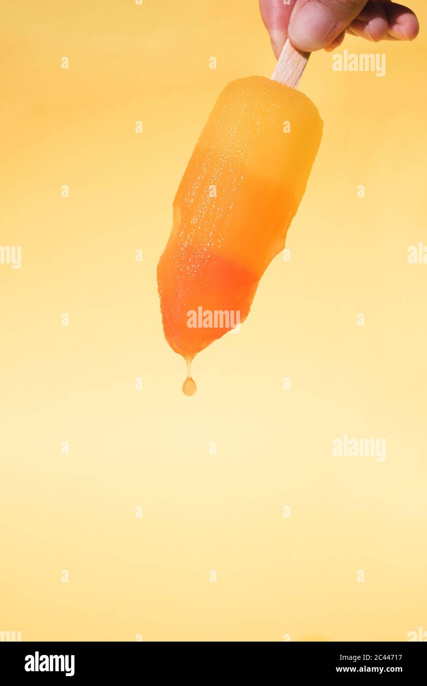 cropped Hand of mid adult woman holding Dripping Popsicle against yellow background Stock Photo