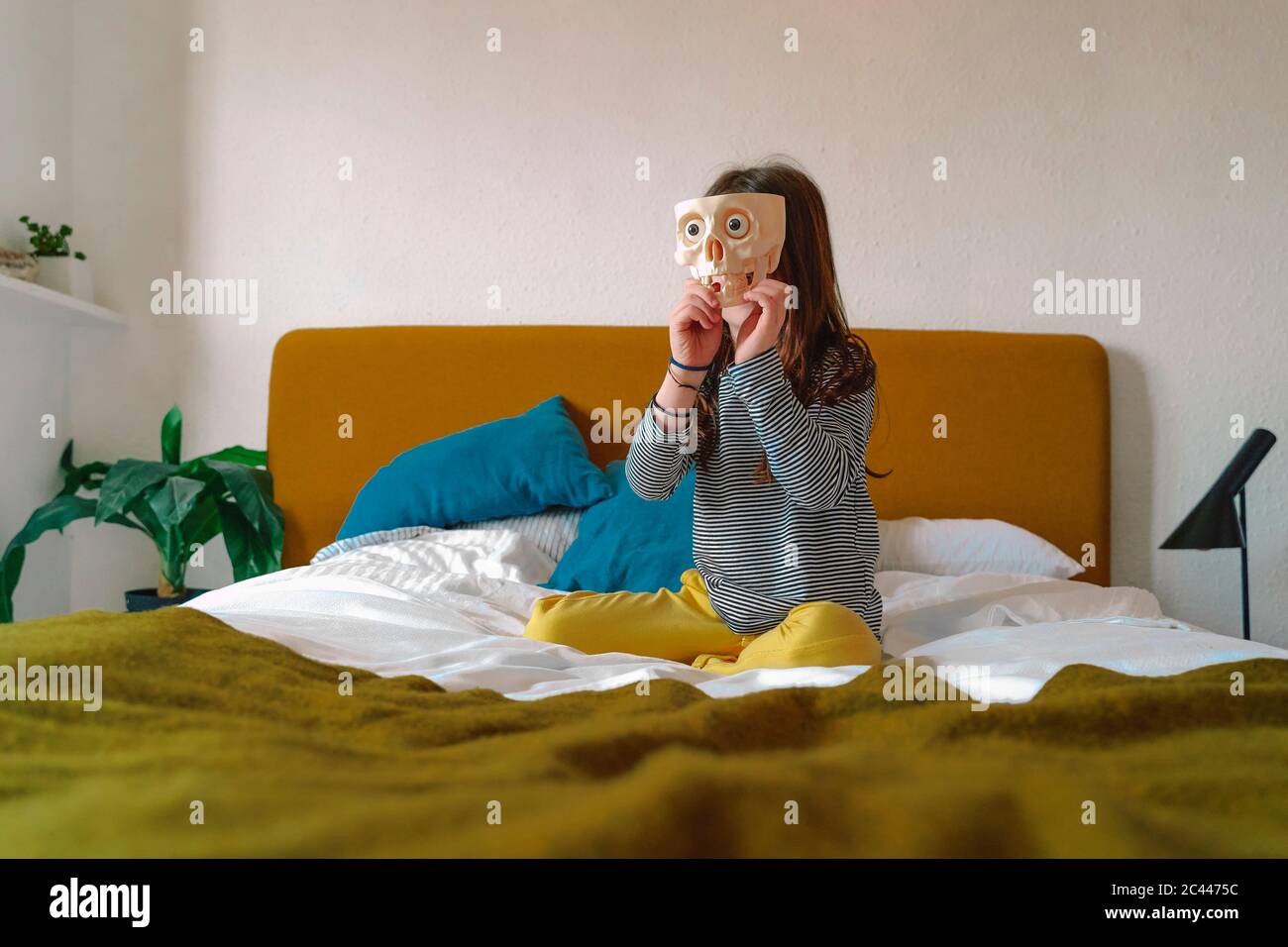 Girl playing with toothless skull sitting on bed at home Stock Photo