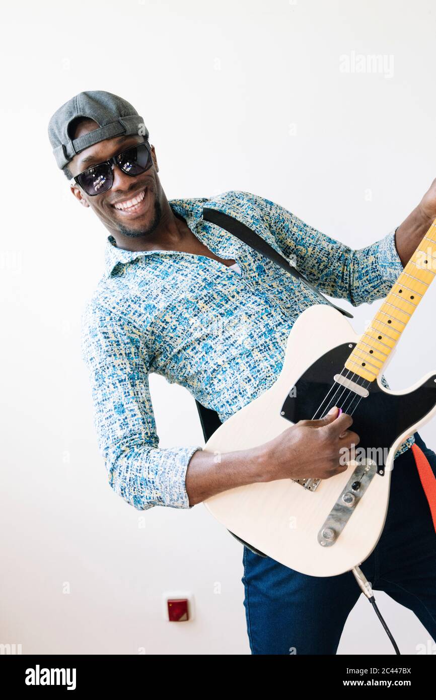 Portrait of happy young pop musician playing guitar against white background Stock Photo