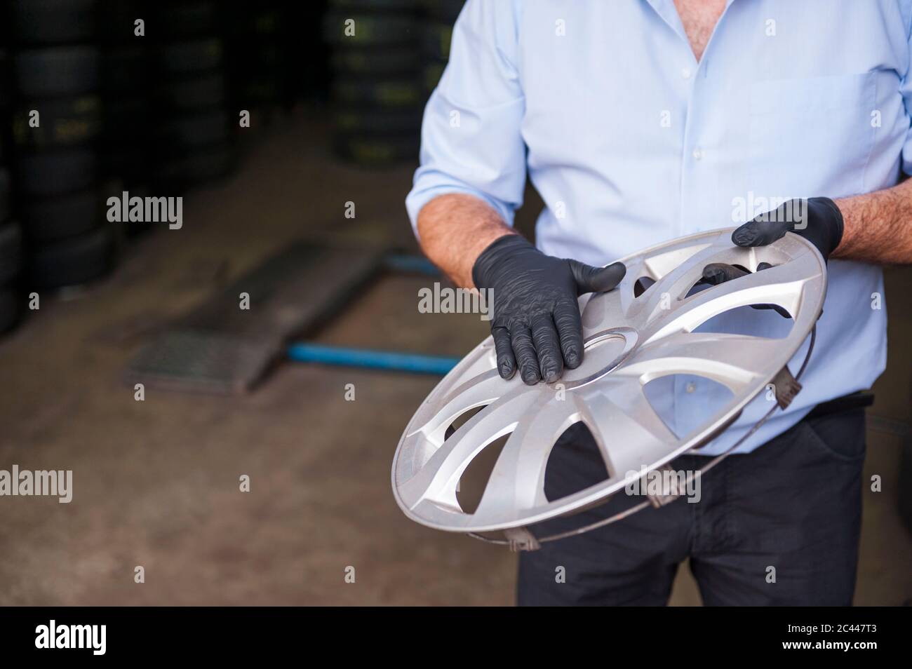 Senior male owner holding hubcap while standing at store Stock Photo