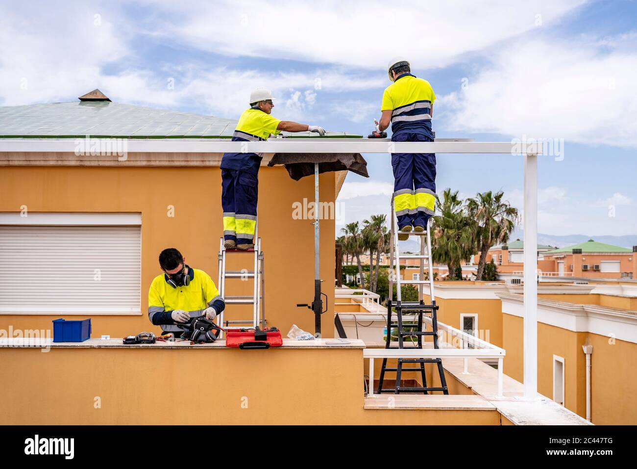 Male technicians installing solar panels on house roof against cloudy sky Stock Photo
