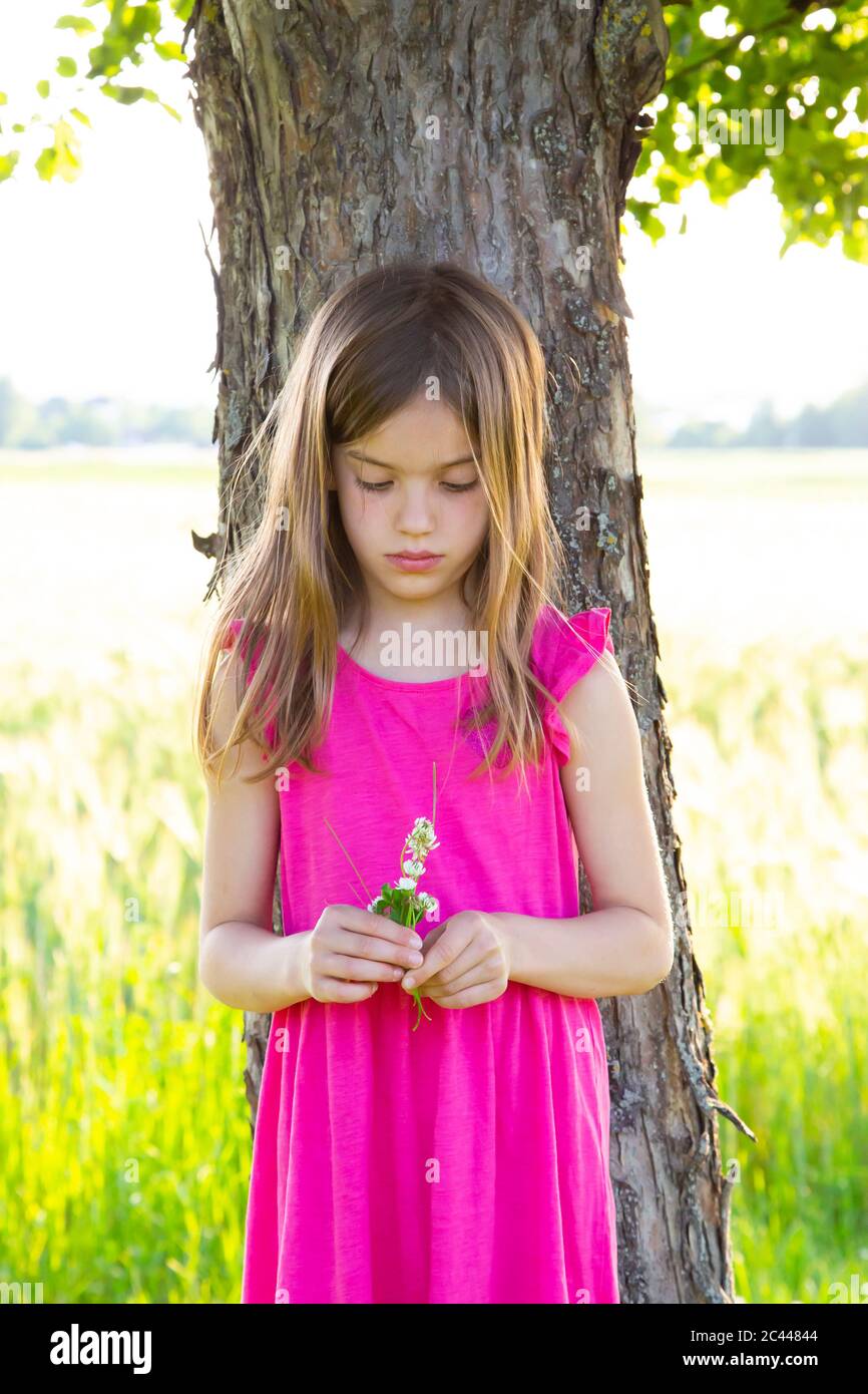 Portrait of little girl standing under apple tree with clover flowers in hands Stock Photo