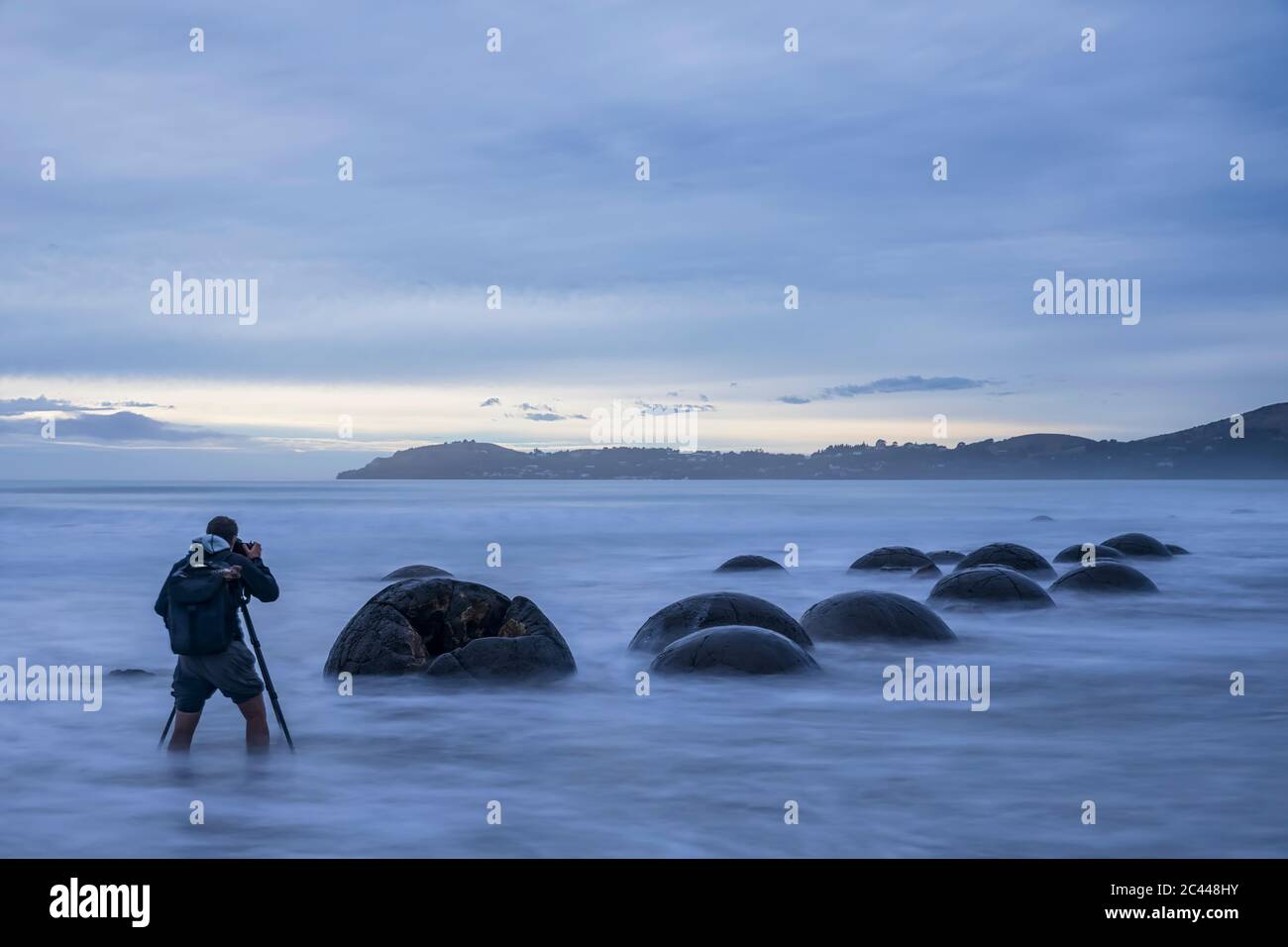 New Zealand, Oceania, South Island, Southland, Hampden, Otago, Moeraki, Koekohe Beach, Moeraki Boulders Beach, Moeraki Boulders, Man photographing round stones on beach at dusk Stock Photo