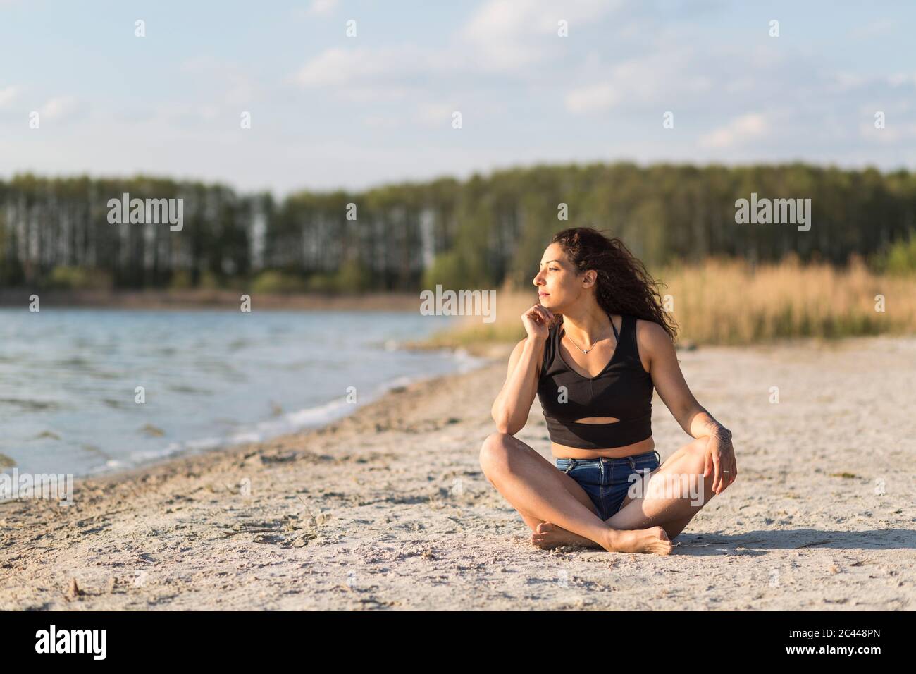 Young woman sitting on the beach looking at distance Stock Photo