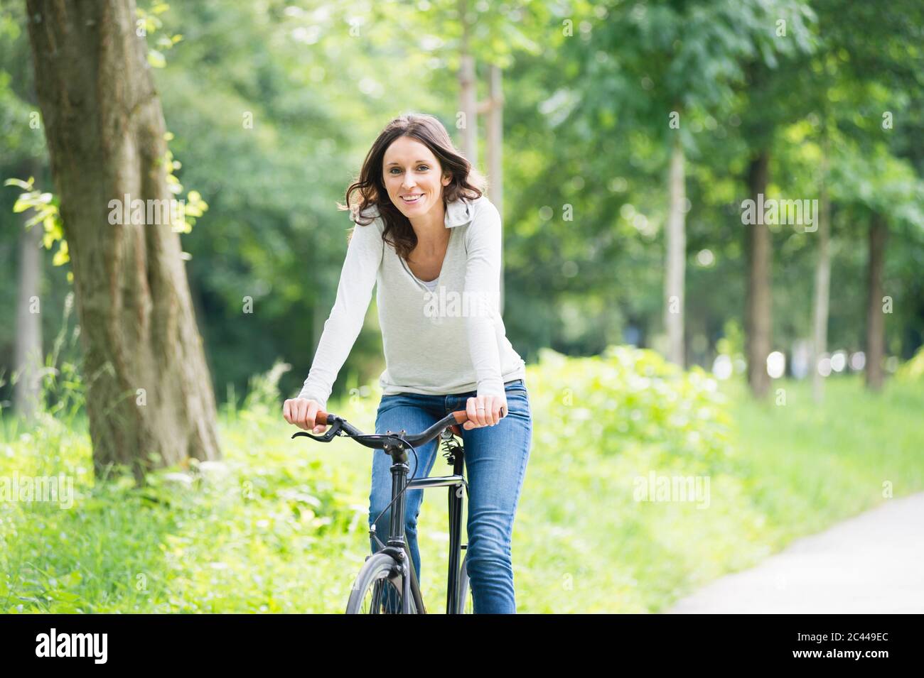 Happy young woman cycling against trees at park Stock Photo