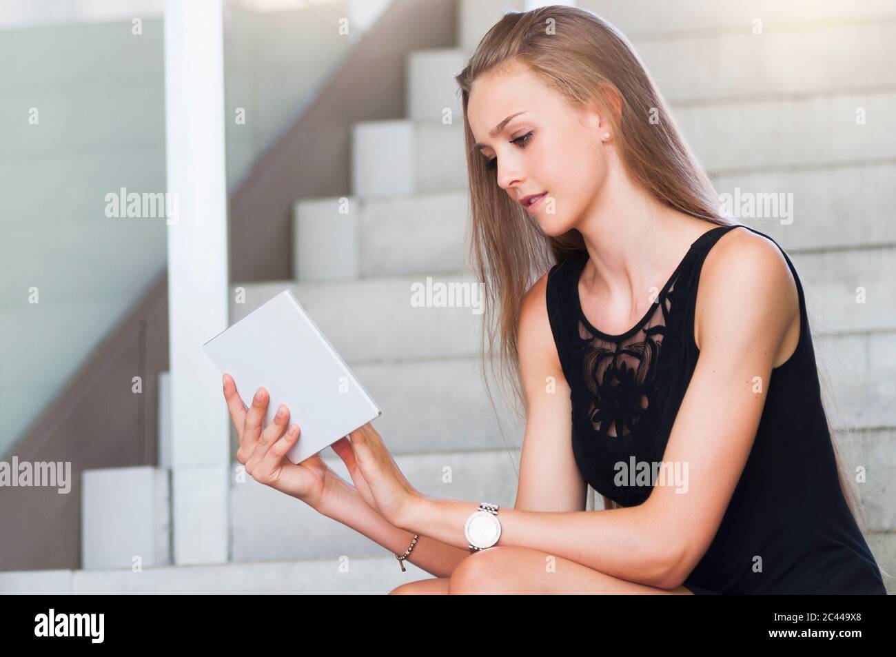 Portrait of young woman sitting on stairs using mini tablet Stock Photo ...