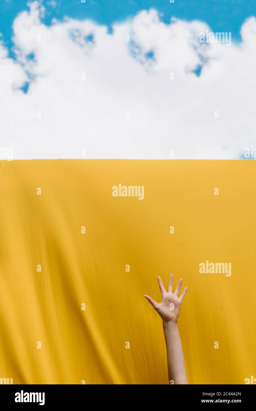 Woman's hand over yellow wall against cloudy sky Stock Photo