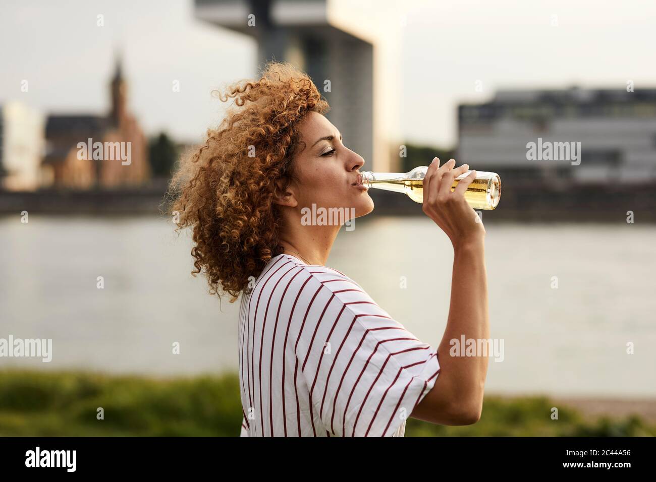 Portrait of smiling woman drinking from glass bottle at riverside Stock